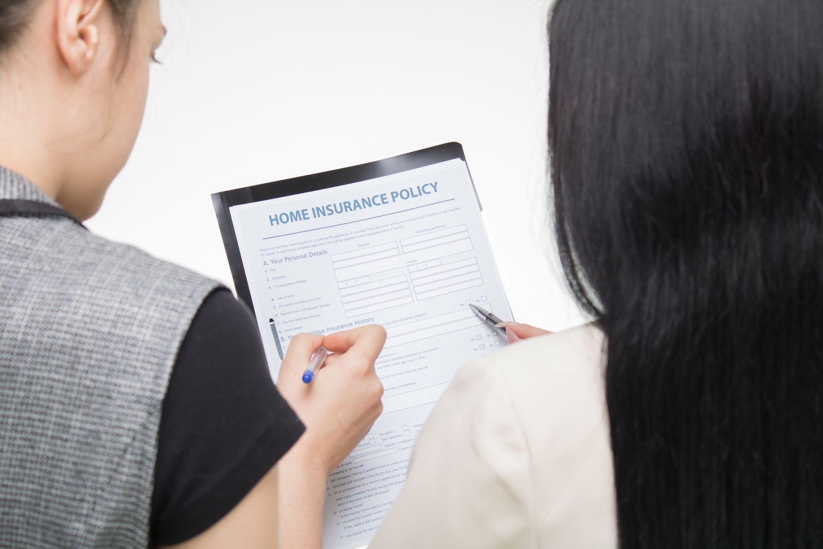 Two women examining home insurance policy form, focused on details.
